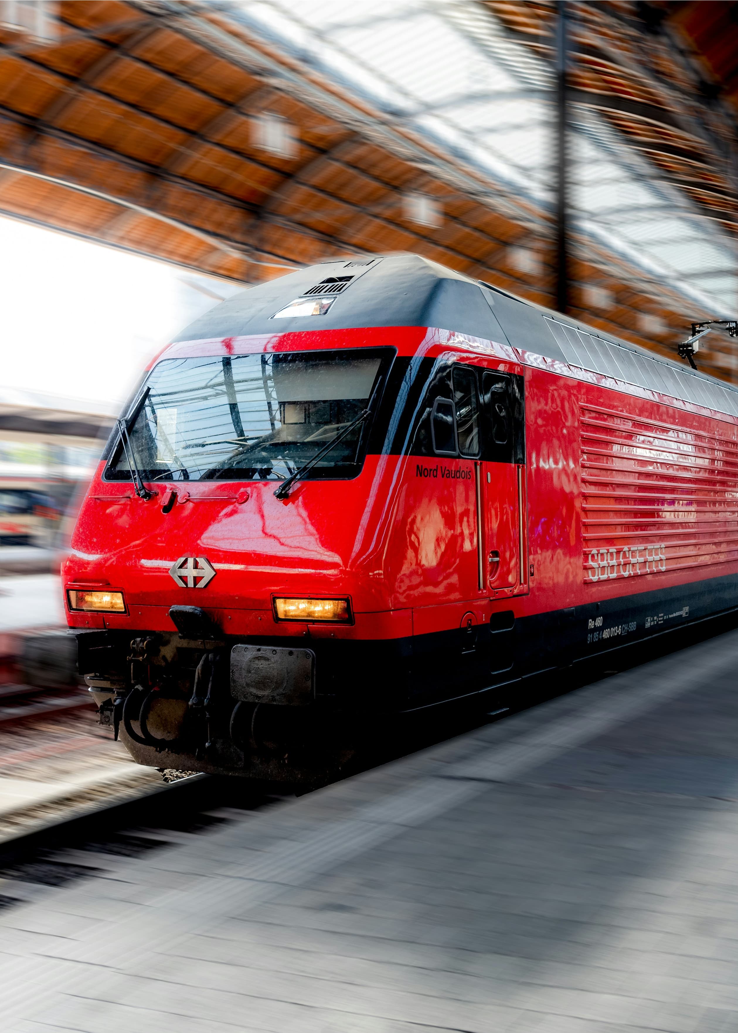 A red Swiss train pulling into a covered station platform, captured with a sense of motion.